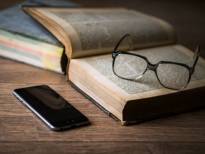 A phone and an open book with glasses on a table