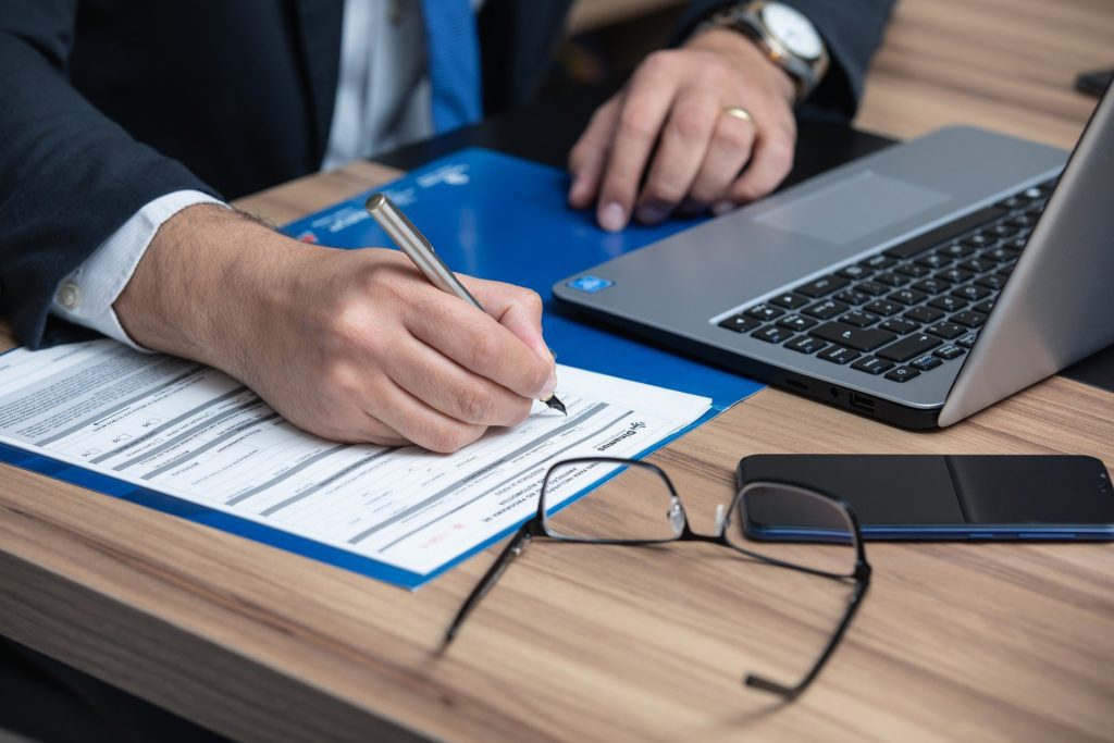 A man doing paperwork at his desk with a laptop and a smartphone