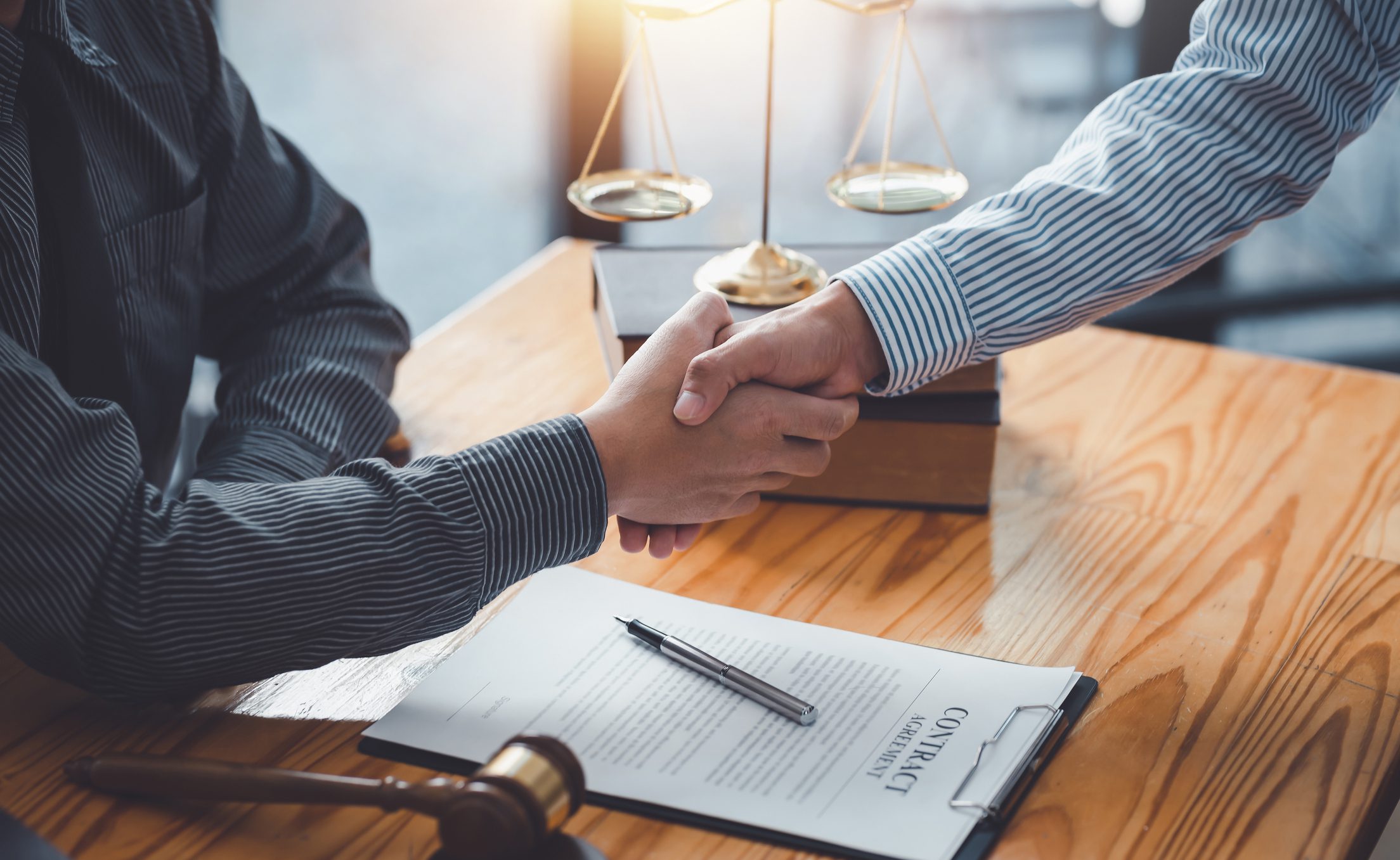 Two people shaking hands over a desk with a contract on it