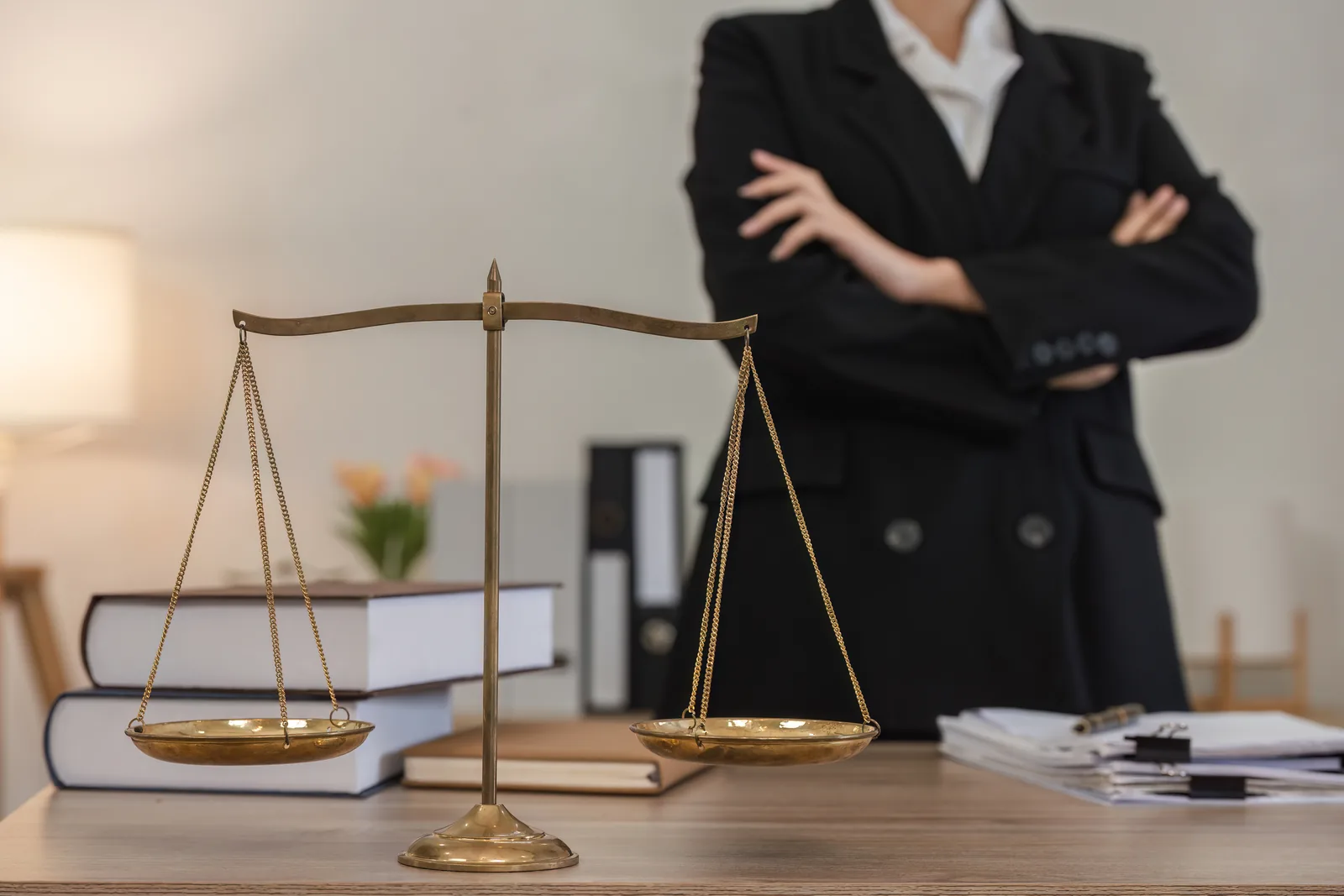 Brass scales of justice on a law firm desk, with legal books and a lawyer standing out of focus behind them