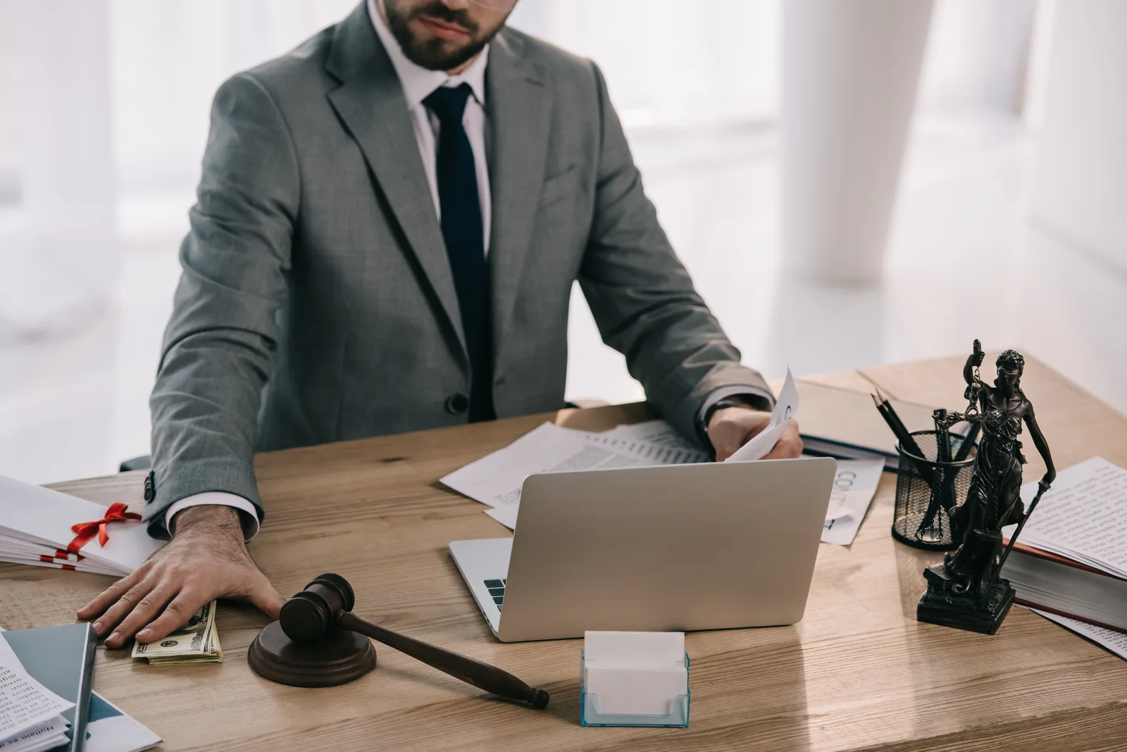 Employment lawyer reviewing documents at a desk with a laptop, gavel and a statue of Lady Justice