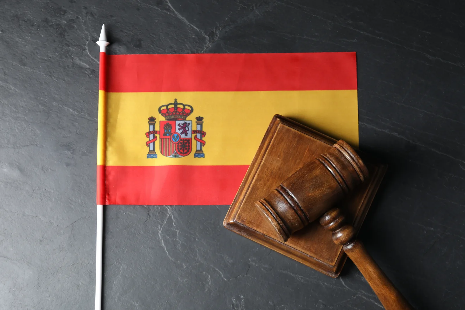 Spanish flag beside a wooden gavel on a dark slate surface