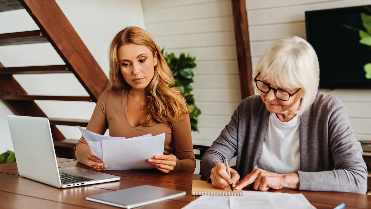 Elder law firm content: adult daughter and senior mother reviewing papers at a table