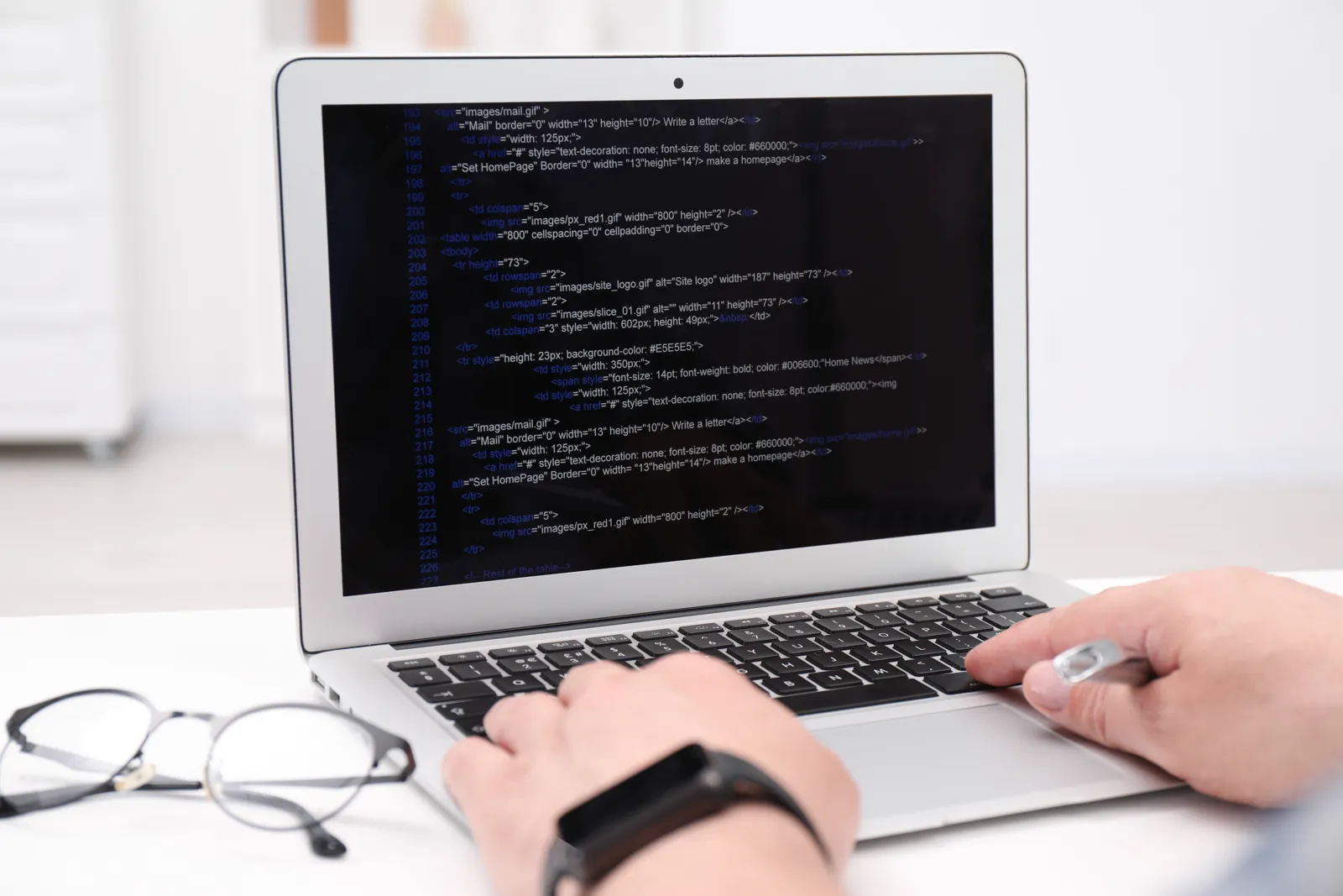 Hands typing HTML code on a laptop at a desk