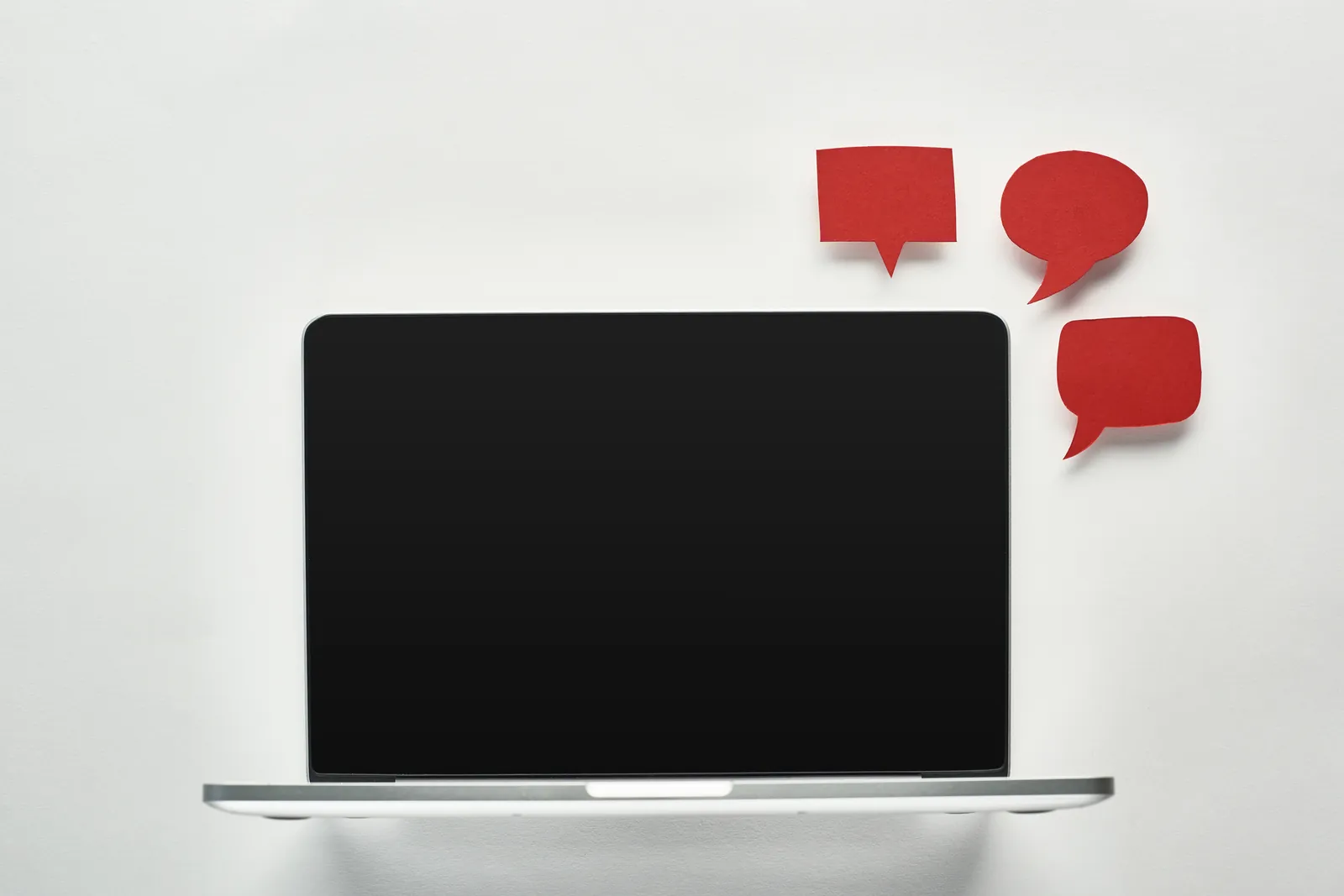 Laptop on a white surface with red paper speech bubbles